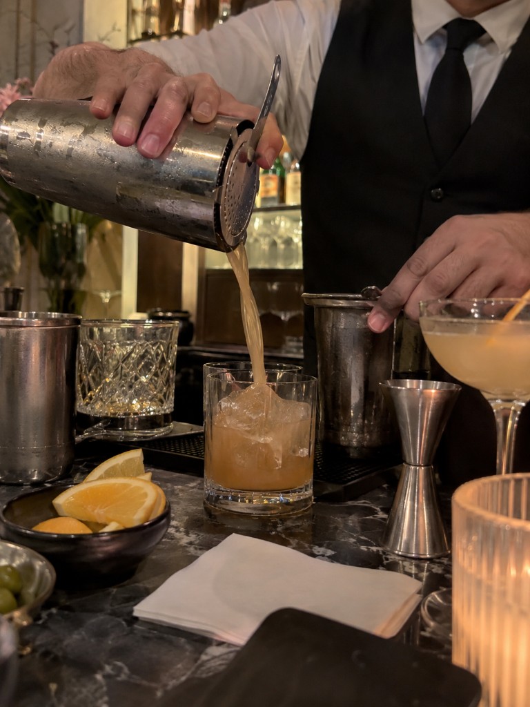 Bartender pouring a shaken cocktail over ice into a rocks glass
